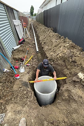 man working in trench checking level of a man hole pipe with a spirit level