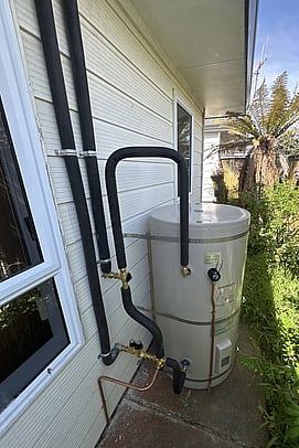 outdoor rinnai hot water cylinder with insulated pipes running up the wall of a house