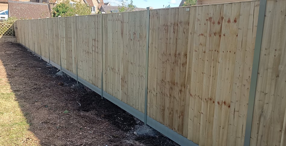 Image shows a completed Durapost fence install comprising Olive green posts, composite gravel boards, cover strips and post caps. Closeboard type panels were used, supplied in light green Tanalith treatment.