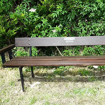 An old style 3 seater bench installed into grass verge area.