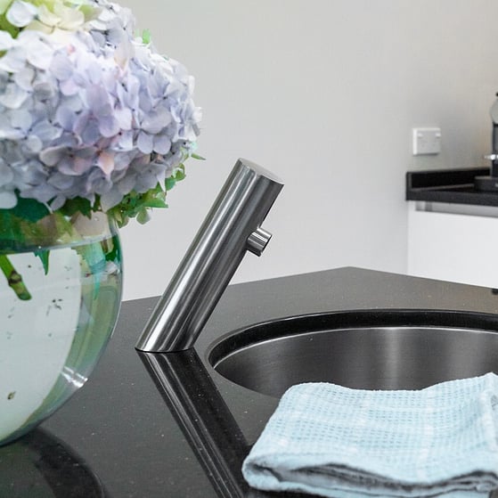 The stylish ET2-97 installed over a stainless steel insert sink as part of a kitchen hand washing area. Black granite work top and vase of flowers to the left.
