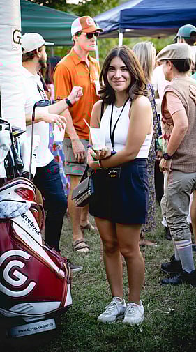 Woman standing next to golf bags at an outdoor Daddy Shack golf event