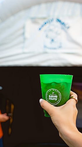 Close-up of a hand holding a green Save Muny branded cup at a Daddy Shack golf event