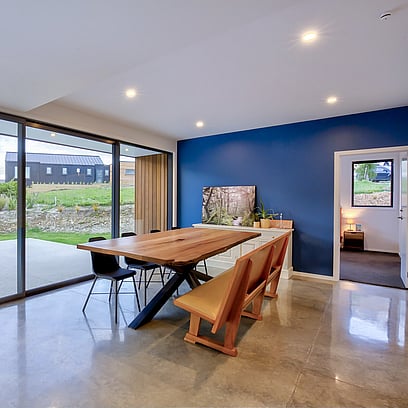 Dining area with s polished concrete floor, wood dining table and blue feature wall.