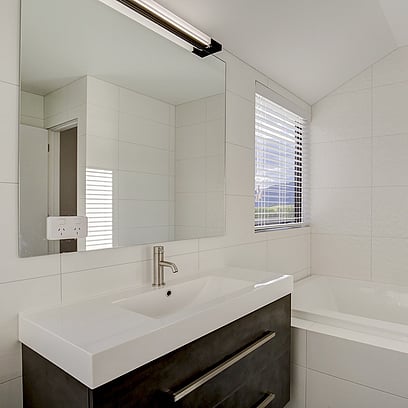 A fresh and modern bathroom with white tiled walls, dark vanity with light basin, large mirror and bath.