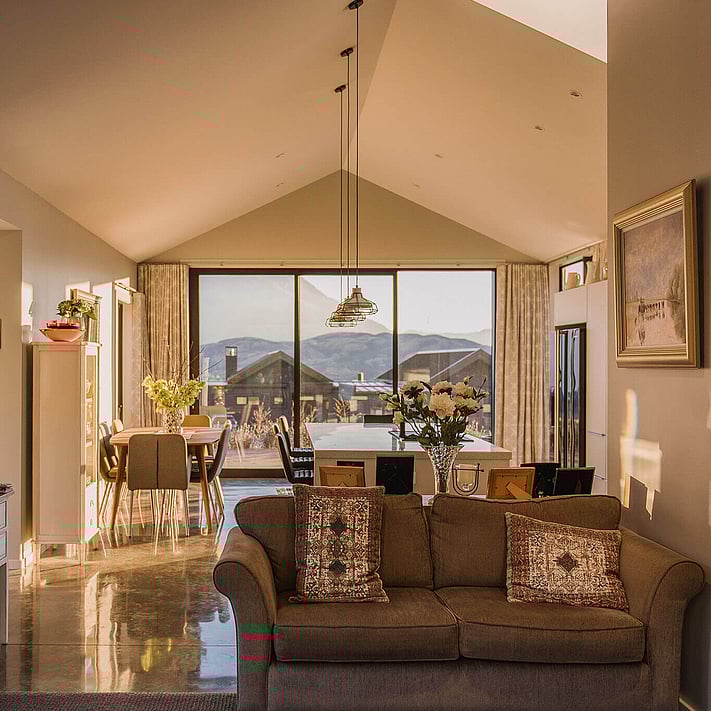 Looking out along the living and dining area of the home. Polished concrete floors, warm light and styled furniture.