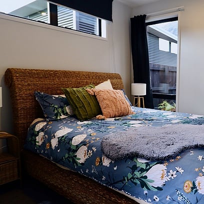 A cozy bedroom with a large bed, light walls, floral duvet and rattan headboard.