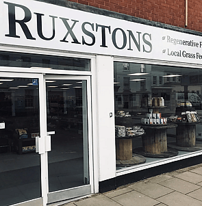 a view of a stream through the woodland with some rushes on the bank in the foreground and the dappled shade of the trees overhead