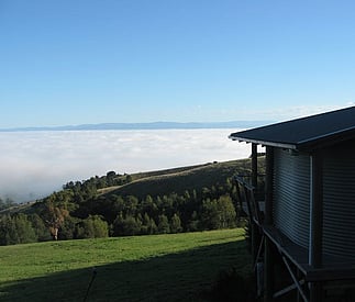 fog in the valley below and blue skies and green grass and trees at the cottage level