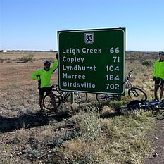 Cyclists beside road sign to Leigh Creek