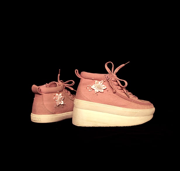 Pink canvas sneaker style pair of boots, with pink satin flower decoration. The boot in the forground has a sole that higher than the other boot. Especially adapted for Indie right leg which is shorter than her left. 