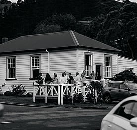 A black and white photo of a wedding party standing on the ramp outside the Kūaotunu Hall