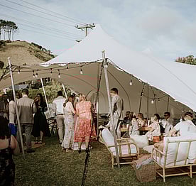 A wedding reception being held in a marquee on the back lawn of the Kūaotunu Hall