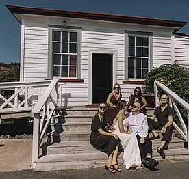 A wedding party posing for a photo on the front steps of the Kūaotunu Hall