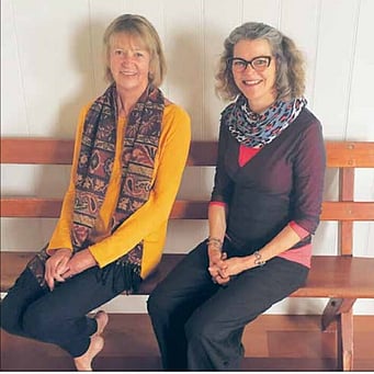 Kūaotunu Hall Committee Member Jo Mullins sitting on a pew in the Kūaotunu Hall with yoga teacher Jose Kakebeeke