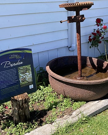 The Heritage Trail sign outside the Kūaotunu Hall which shows a picture of the original Kūaotunu School from where the hall came