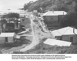 An historic black and white photo showing the lower town main street of Kūaotunu circa 1900