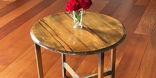 A small cake table with a vase of roses on it, standing on the wooden floor of the Kūaotunu Hall