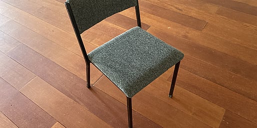 A grey chair with black metal legs standing on the wooden floor of the Kūaotunu Hall