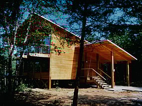 Modern heavy timber post and beam house with cedar siding. View from Southeast showing carport and front entry.