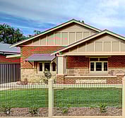 View from front yard of red brick bungalow with cream and tan paint. Restored bungalow featuring new window canopy, restored sandstone, corrugated metal roof, period fencing, period lighting and new paint scheme.