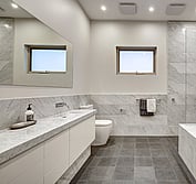 Interior view of large bathroom with marble vanity, toilet, undermount bathtub and open shower. Main Bath with honed Carrara marble wall tiles and vanity with cut in sink. Honed black granite floor tiles.