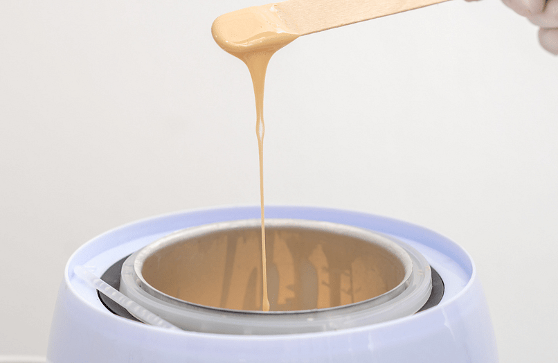 Image of wax dripping from stick above hot pot of wax