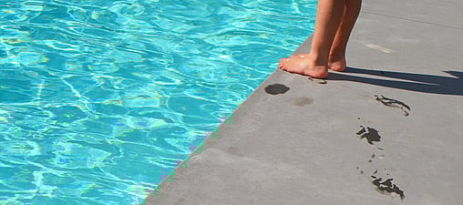Image of cropped legs standing next to a cropped in part of a swimming pool