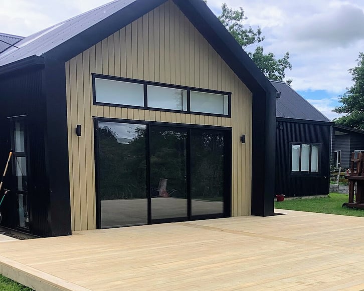 Image of newly built timber deck and dark cladded home with light timber accent and dark joinery. Decking by Coull Builders, Otorohanga.