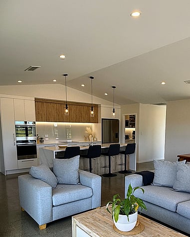 Image of newImage of light modern kitchen with timber accents, and peak of grey lounge suite. Building by Otorohanga builders, Coull Builders.