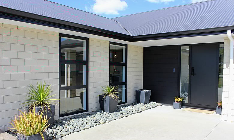 Image of large stone coloured brick home with dark roofing, doors and joinery. New home by Coull Builders, Otorohanga.
