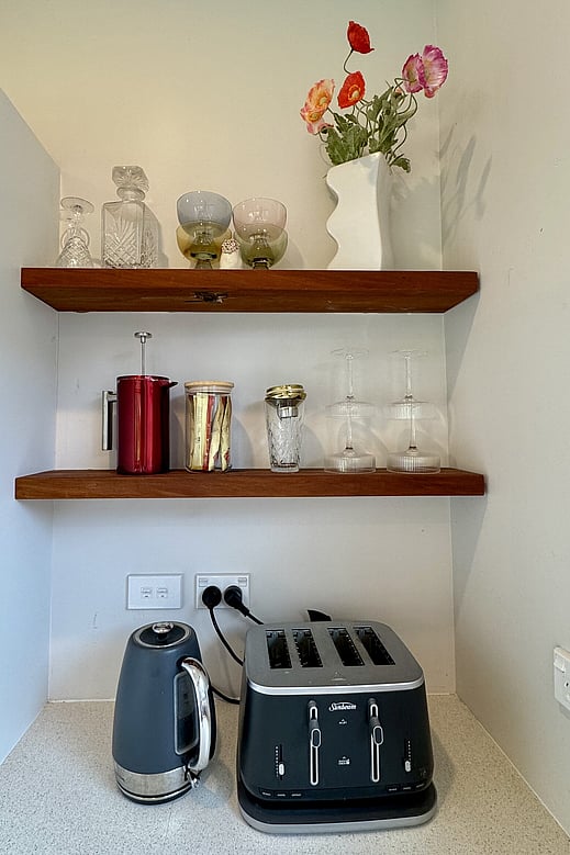 Image of rustic wooden floating shelf with decorative glasses, whiskey decanter and flowers. Renovation by Coull Builders, Otorohanga, Waikato.