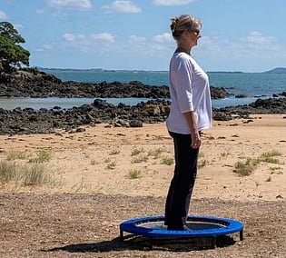 Woman with correct posture, health bouncing on a XenPod Lymphaciser wellness mini-trampoline at the beach