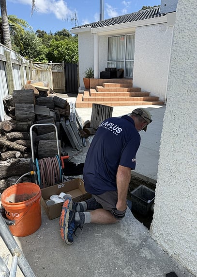 plumber wearing navy blue tee with a plus branding performing maintenance on an outside drain by a patio