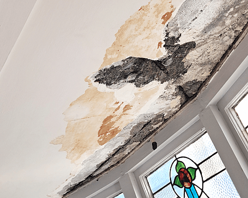 Cracked concrete ceiling and water-damaged plaster next to stained glass window.