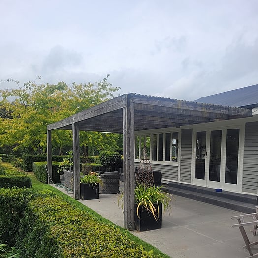 An old pergola on front of a grey weatherboard home.