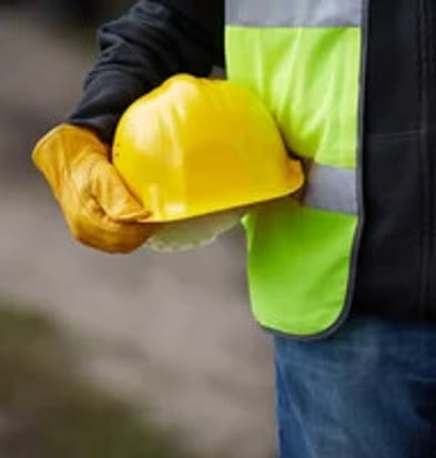 Construction worker holding yellow safety helmet and gloves onsite