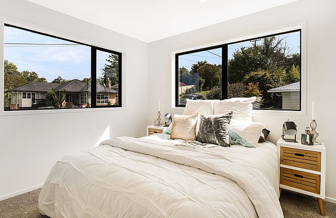 Image of a residential new build home. Sunlit bedroom with queen bed. Built by Auckland builders, Eden Construction. New Zealand.