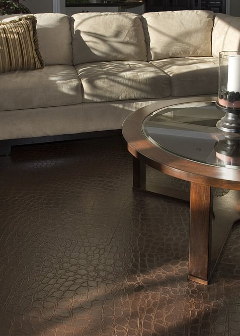 A textured brown leather floor with a beige sofa and brown glass top coffee table. 