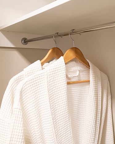 Two white robes hanging on wooden hanger on a wardrobe rail.