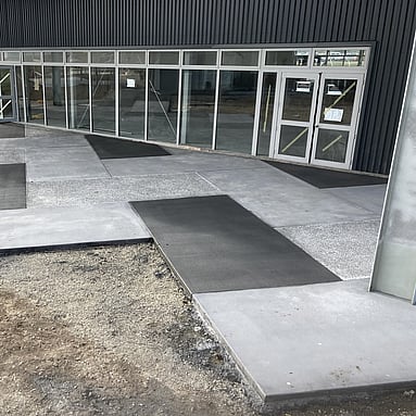 Outdoor concrete surrounding a school building, using three different types of concrete: dark grey, light grey, and exposed aggregate 