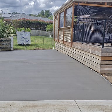 smaller smooth grey concrete driveway next to house with wooden patio  