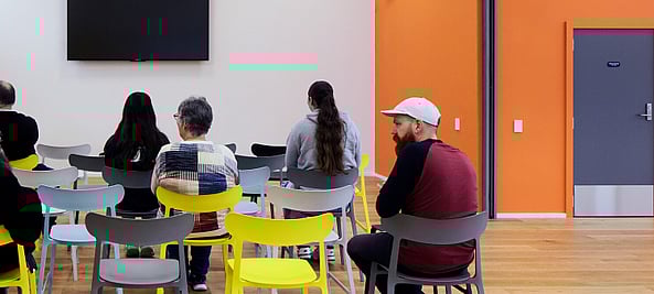 picture from behind of people using one of our activity rooms. There is a wall mounted TV in the background.