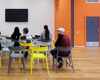 picture from behind of people using one of our activity rooms. There is a wall mounted TV in the background.