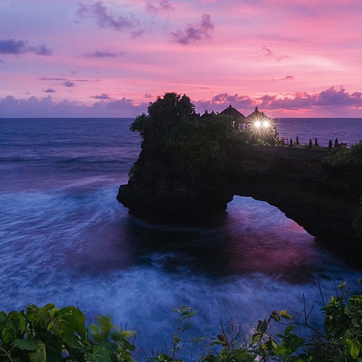 Tanah Lot temple at sunset with blue ocean and pink sunset.