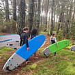 Young people walking through the forest holding surf boards