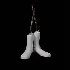 A pair of white boot/feet shapes made of plaster. Each with a nylon stocking sheath stretched over it and knotted at the top where a steel reinforcing rod protrudes out of the boot shape. These boot shaped plaster objects stand as a pair on a square black back ground. 
