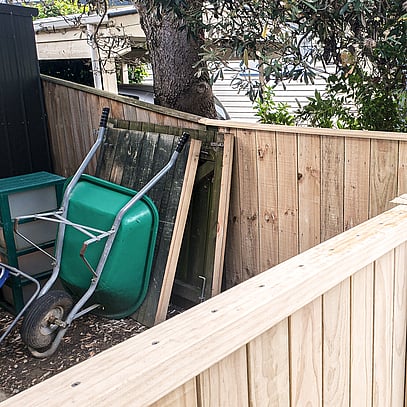 Wooden light coloured fence and green wheelbarrow.