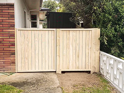 Wooden Gate built in between a House and a fence.