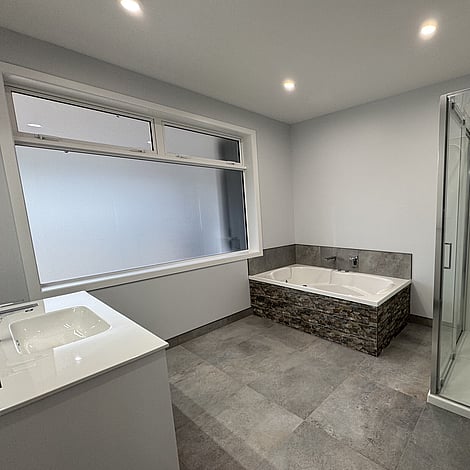 Image of tiled floor bathroom with stone edged bath in Te Wharepu Road new home build. Built by Ardent Building Developments, Hamilton. Waikato, New Zealand.